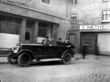 Paul Netheim 1928 am Steuer seines Autos; im Hintergrund die Rosenstraße mit der Seitenansicht des Geschäfts  